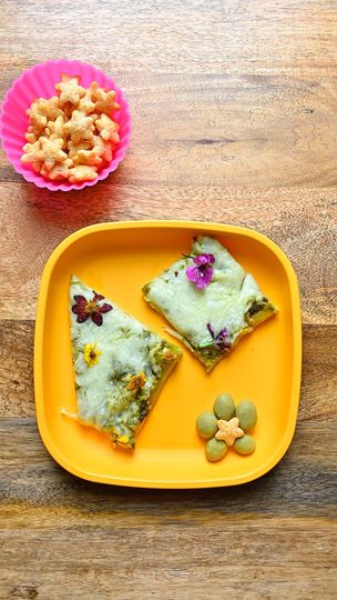 Two slices of herb-topped focaccia on an orange tray, accompanied by snacks, on a wooden table
